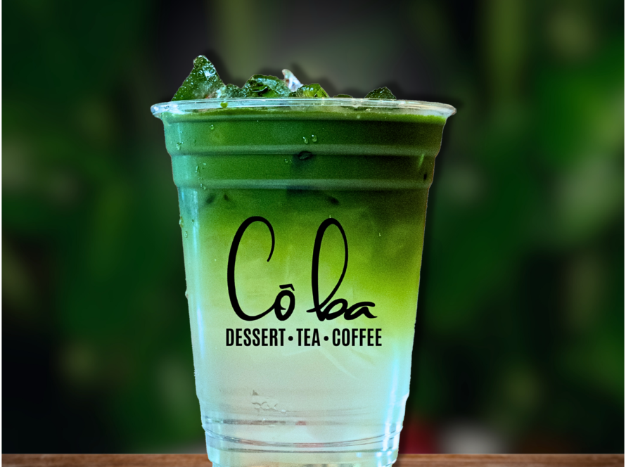 A cup of green drink with ice sits on a table, showcasing the word 'BLISS'.
